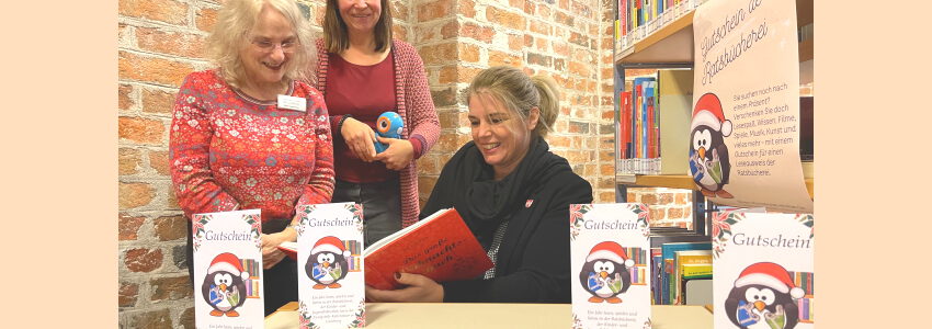 Foto: Hansestadt Lüneburg. Gute Idee zu Weihnachten: ein Gutschein für die Ratsbücherei birgt ein Jahr lang tolle Möglichkeiten. Oberbürgermeisterin Claudia Kalisch (rechts) unterstützt die Gutschein-Aktion von Evelin Bornmann (links), Antje Bechly (Mitte) und dem Bücherei-Team.