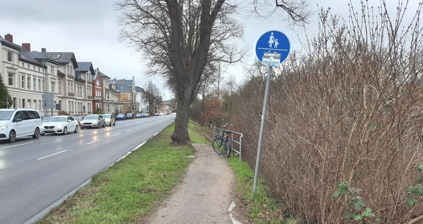 Foto: Lüne-Blog. Das ist der benutzungspflichtige(!) Radweg auf der Ostseite der Schießgrabenstraße zwischen Scharf- und Scholze-Kreuzung: Ein gemeinsamer Pfad - die Bezeichnung Weg wäre hier übertrieben - für zu Fuß Gehende und Radfahrende. Der stark abschüssige Weg führt hier hinunter zum Ilmenaufer und bei der Scholzekreuzung wieder nach hinauf auf Straßenhöhe. Bei Bei diesem Verkehrszeichen 240 müssen Radfahrende besondere Rücksicht auf Personen zu Fuß nehmen und ihre Geschwindigkeit entsprechend anpassen. 