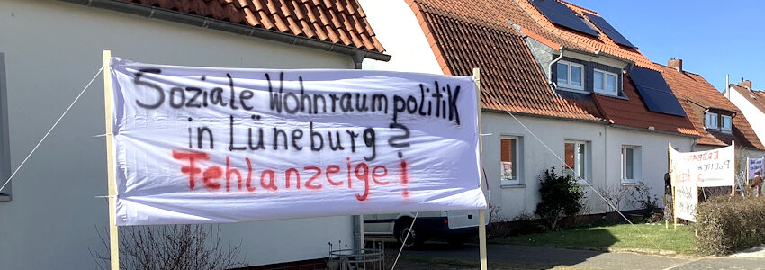Banner "Soziale Wohnraumpolitik in Lüneburg? Fehlanzeige!" vor einem Wohnhaus. Foto: Initiative "Bezahlbarer Wohnraum im Erbbau Lüneburg", März 2025.
