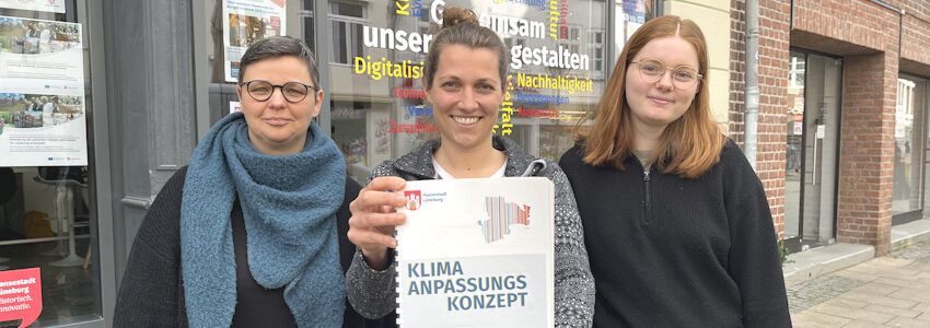 Foto: Hansestadt Lüneburg. Vor dem Dialograum Innenstadt in der Grapengießerstraße stehen, von links: Juliane Ette und Amelie Grunenberg aus dem Team Klimaanpassungs-Management und Marlene Sehrbrock, die im Rahmen ihres Studiums ein Praktikum bei der Hansestadt absolviert.