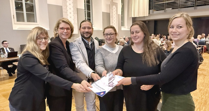 Foto: Hansestadt Lüneburg. Von links: Eva Kern, Koordinatorin des Bürger:innenrats, Oberbürgermeisterin Claudia Kalisch, die Mitglieder des Bürger:innenrats 2025, Tommy Ziegler, Josefina Budzisch und Franziska Hartmann und - ganz rechts - Bürgermeisterin Jule Grunau mit dem aktuellen Bürgergutachten am 12. Februar 2026.