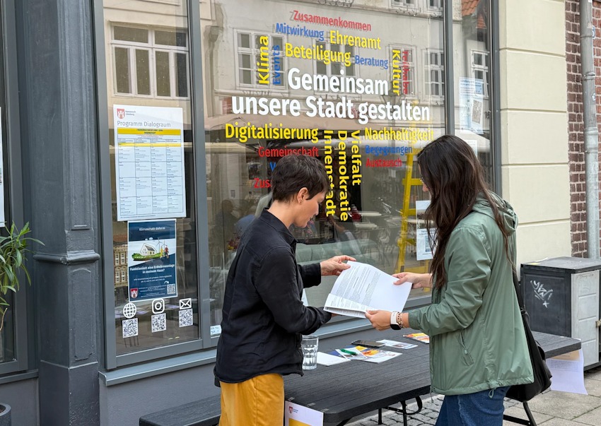 Foto: Hansestadt Lüneburg. Das Wohnraumbüro hat eine regelmäßige Sprechstunde im Dialograum in der Grapengießerstraße. Hier eine Kurzberatung am Infotisch vor dem Dialograum.