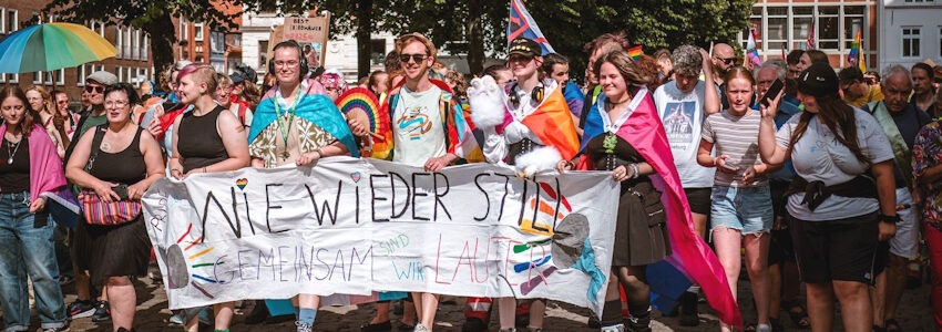 Foto: Ariane Evertz. Pride-Demonstration 2025 auf dem Marktplatz in Lüneburg mit Banner: Nie wieder still!